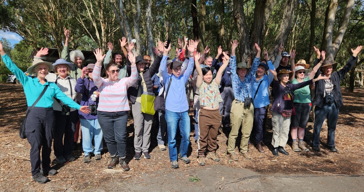 A group of people standing outdoors on a forest path with their arms raised in celebration.