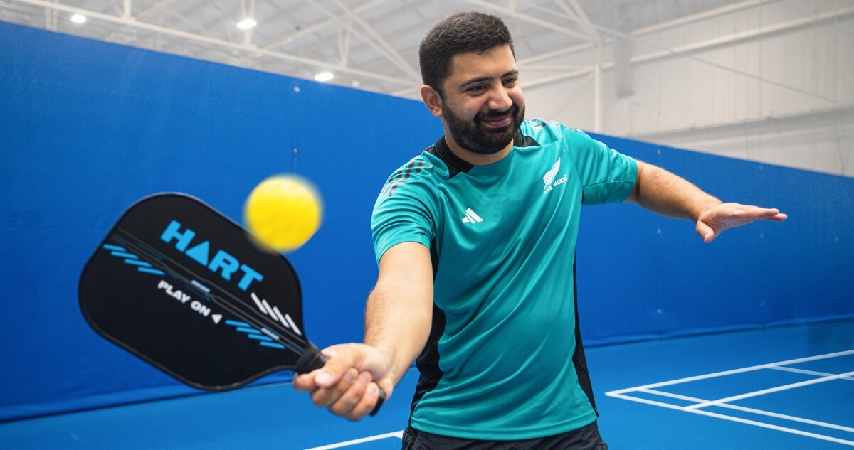 A man hits a yellow pickleball with a paddle on an indoor blue court.